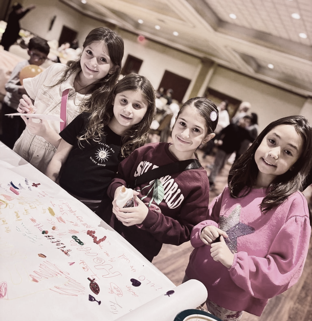 Four smiling children pose around a colorful art project in a bright room.