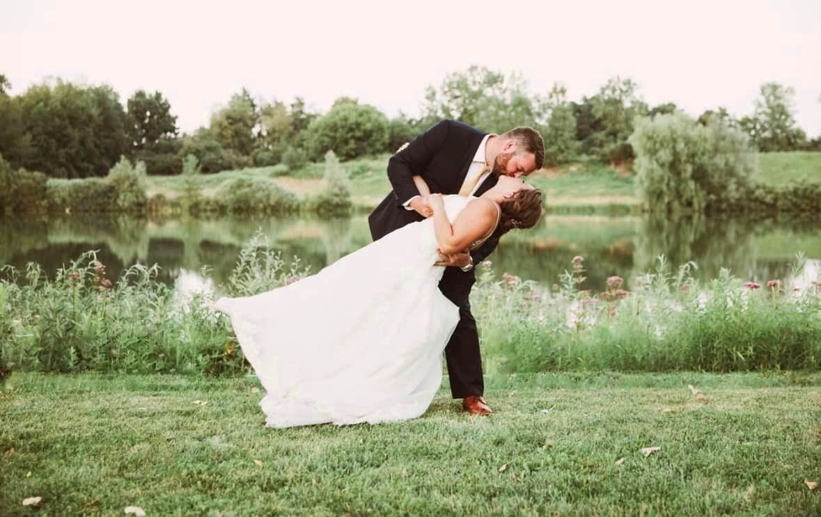 A bride and groom are kissing in front of a lake.