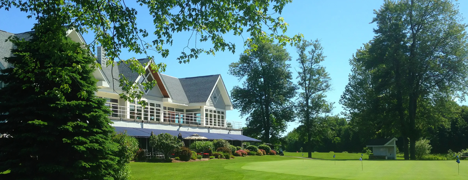 A large house is sitting on top of a lush green field surrounded by trees.