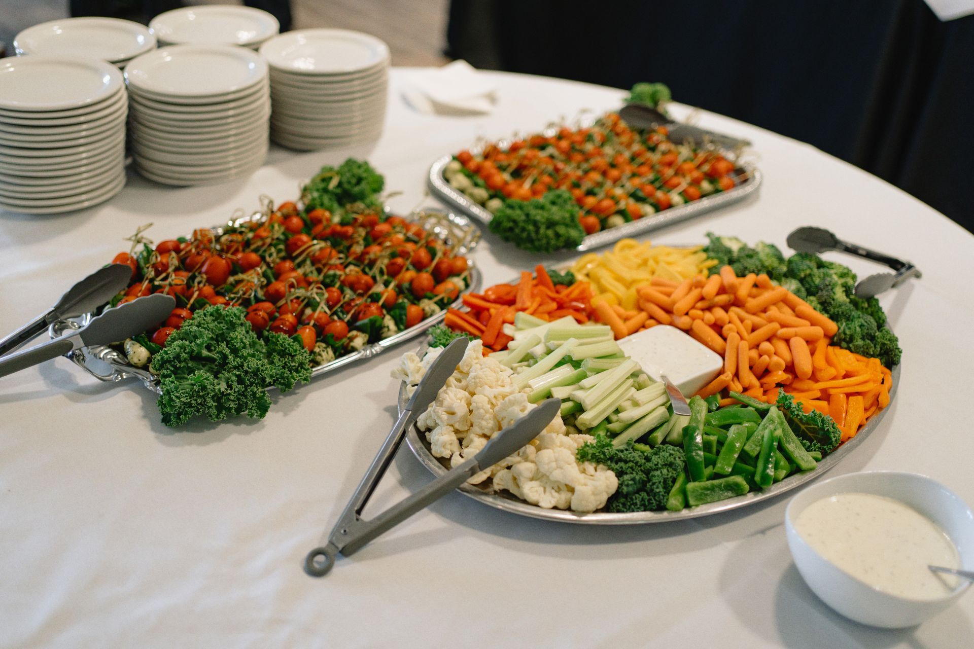 A table topped with plates of vegetables and tongs.