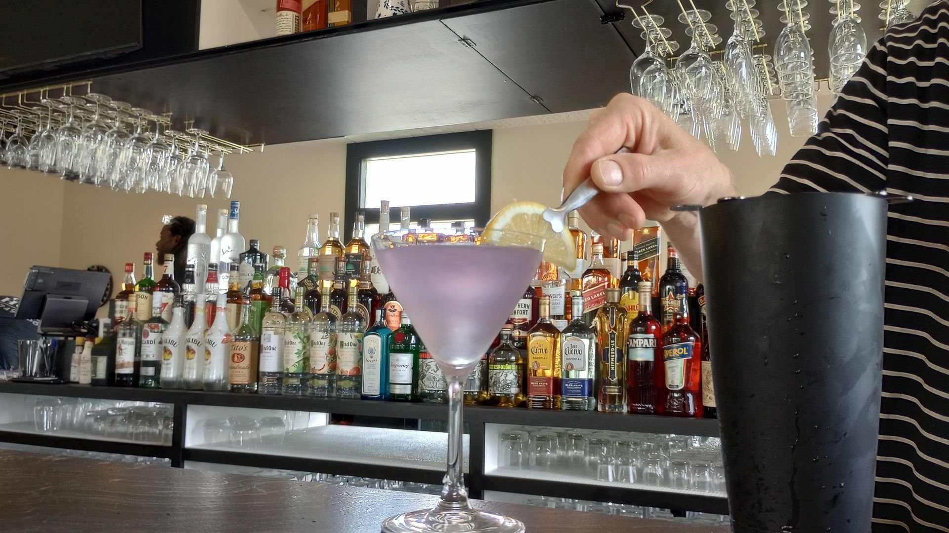 A person is pouring a drink into a martini glass at a bar.