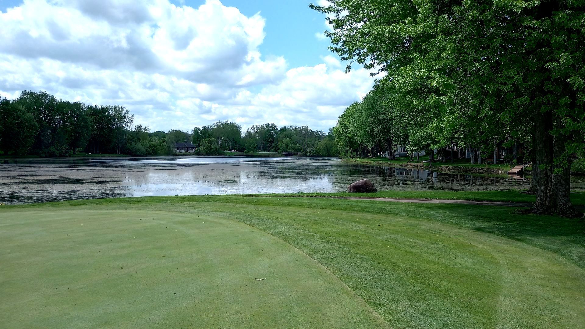 A golf course with a lake in the background and trees in the foreground.