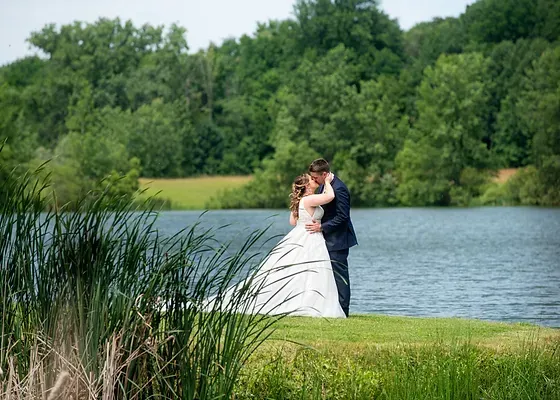 A bride and groom are kissing in front of a lake.
