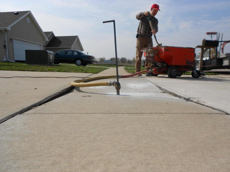 Close-up of a contractor performing concrete raising on a sidewalk, mud jacking a drilled hole.