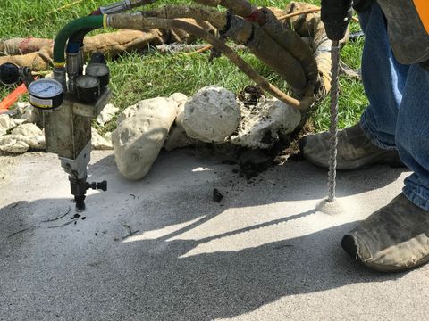 A worker using mudjacking to repair and raise a concrete sidewalk for concrete raising.