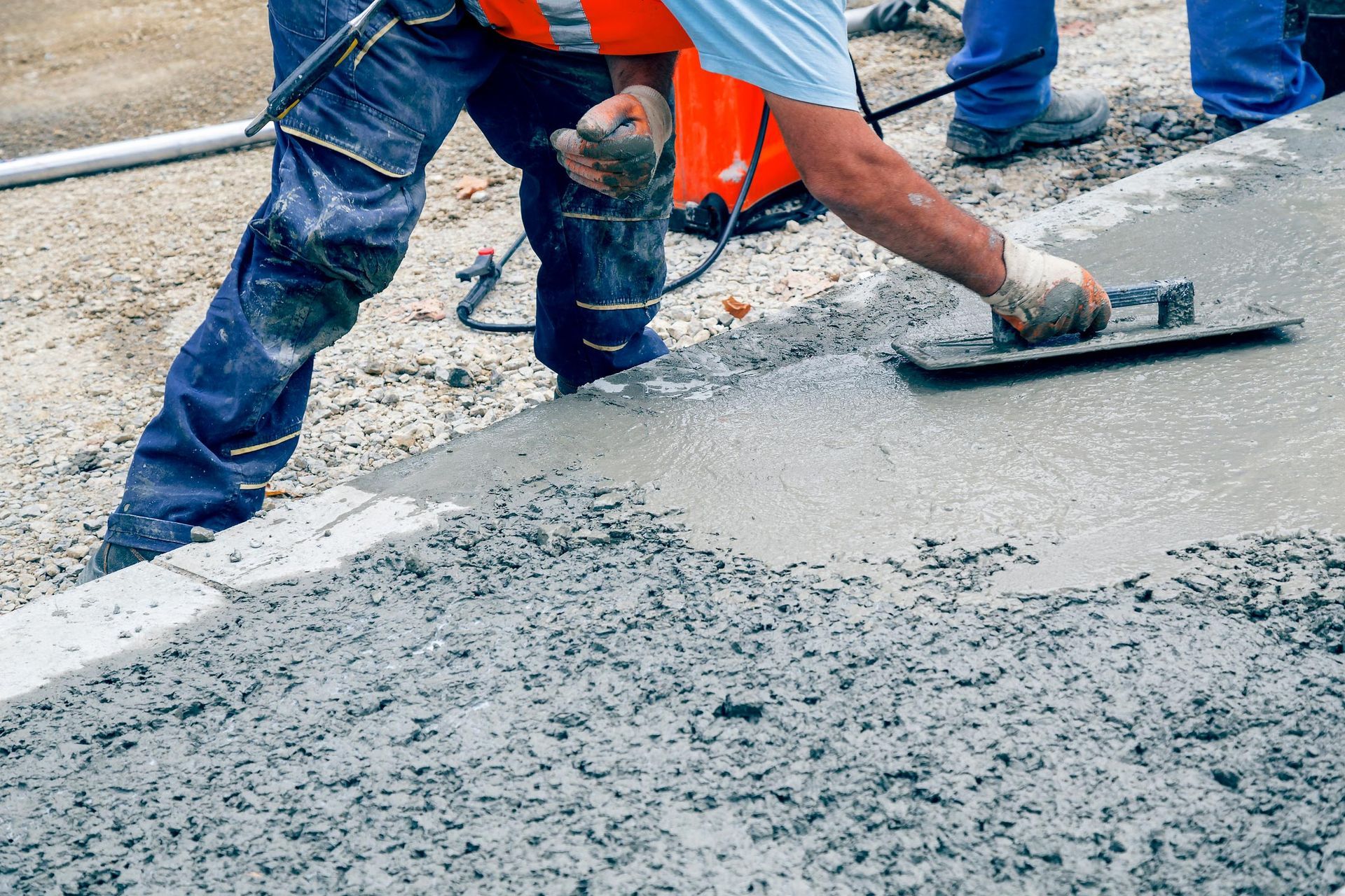 Construction worker smoothing wet concrete with hand float on road surface.