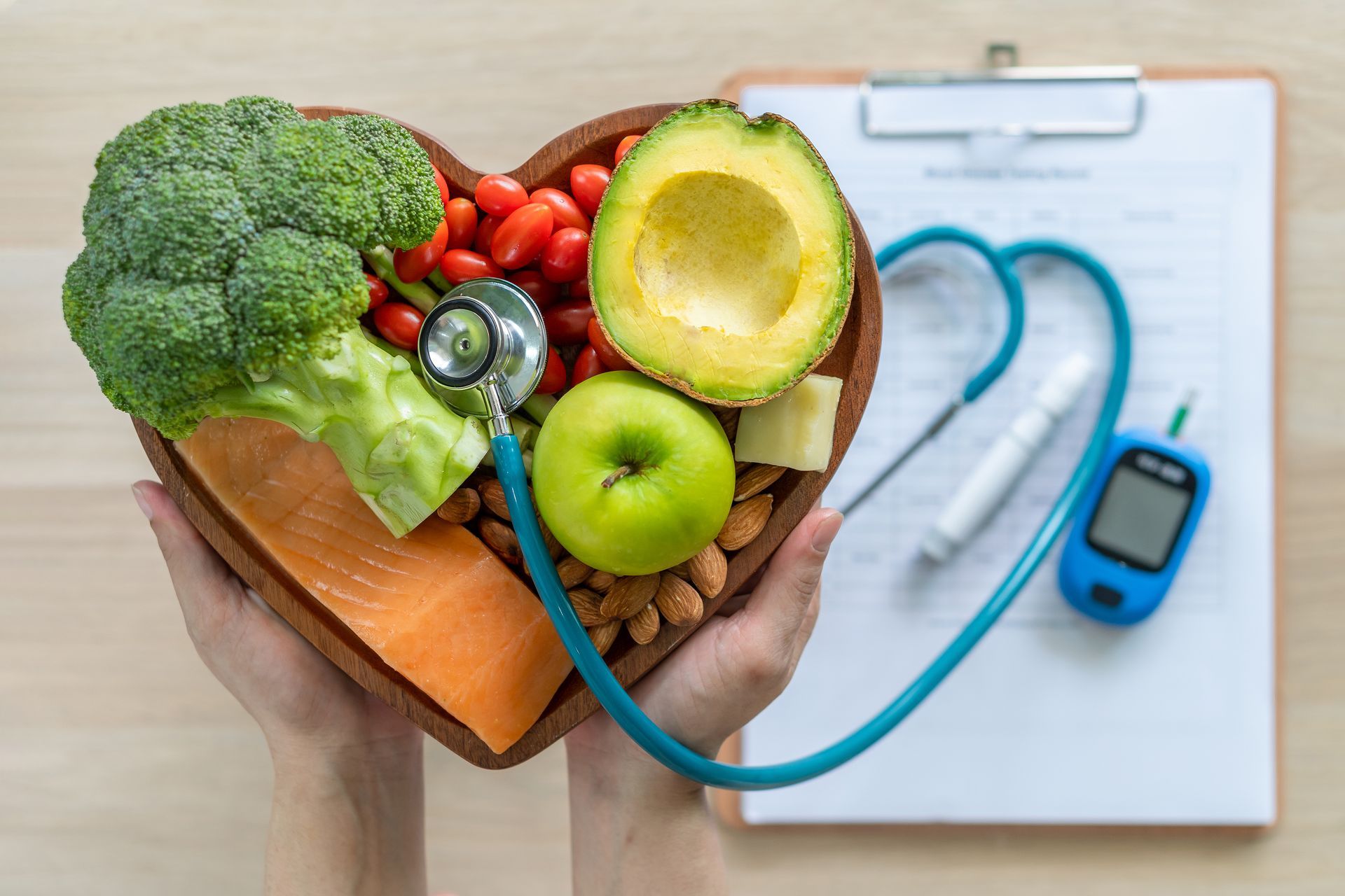 Hands holding a heart-shaped bowl filled with healthy food; stethoscope and medical tools nearby, suggesting health and wellness.