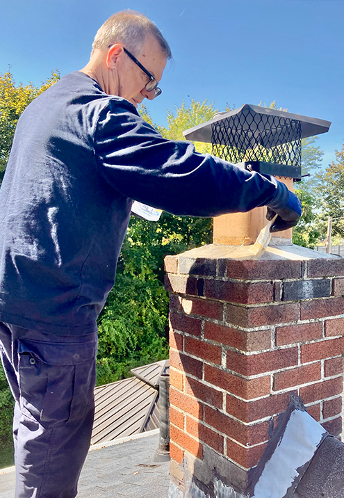Person applying sealant to a brick chimney cap. Bright blue sky.