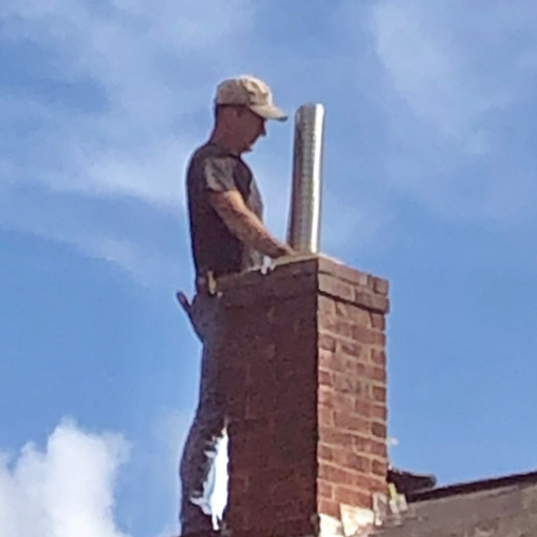 Man on a roof installing a metal chimney liner. Brick chimney and blue sky background.