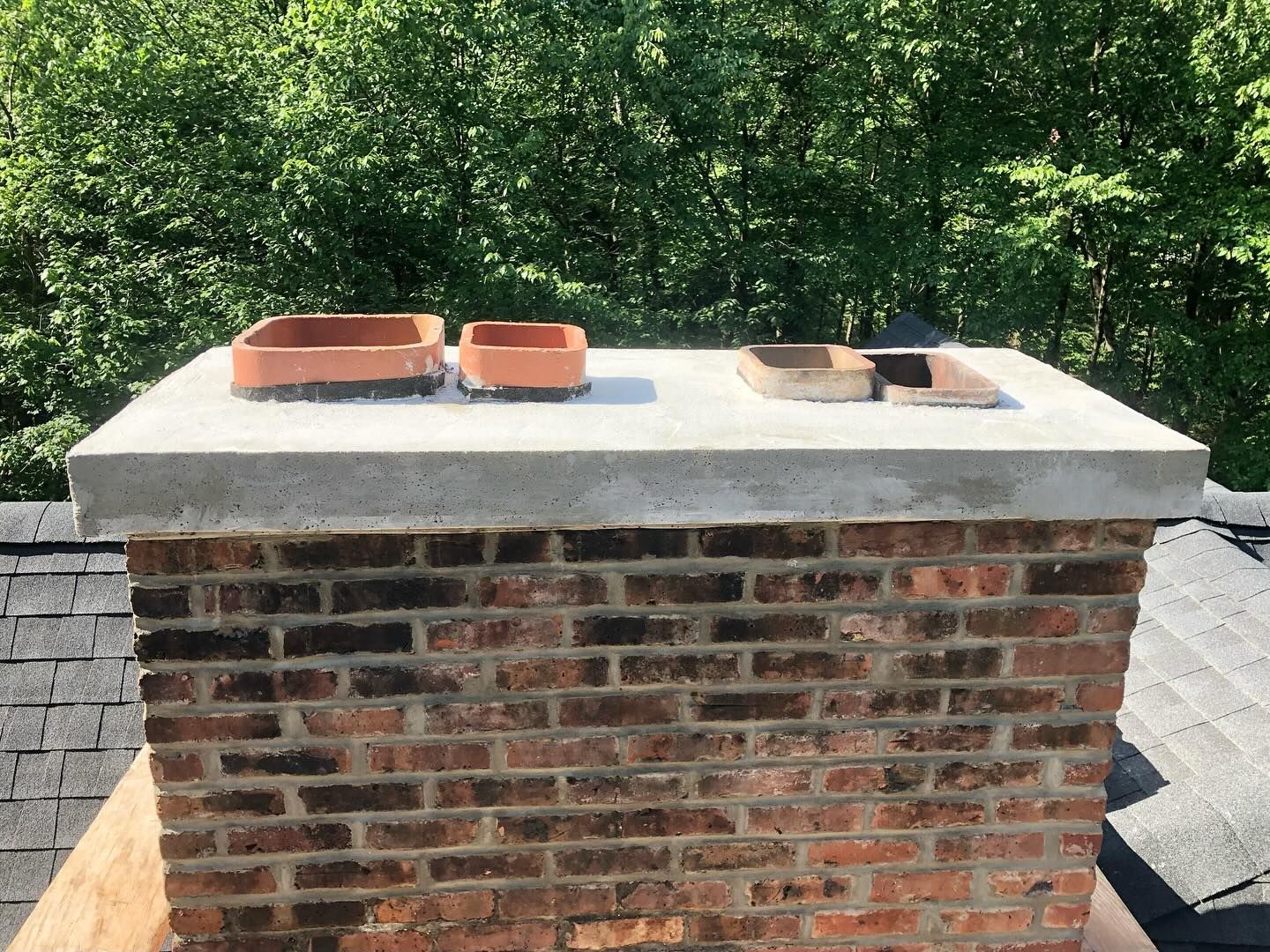 Brick chimney with concrete cap and clay flue liners on a roof.