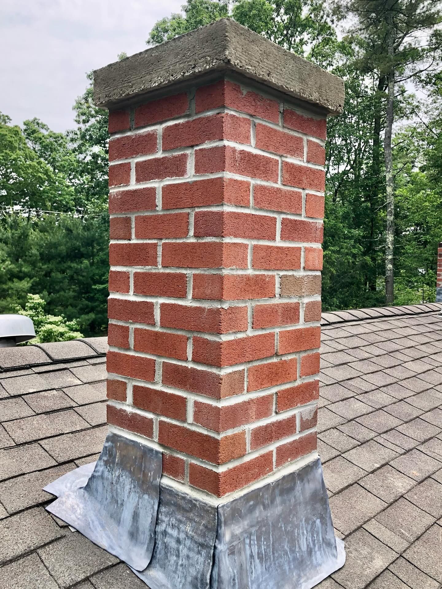 Brick chimney on a shingled roof with a concrete cap. Flashing at the base.