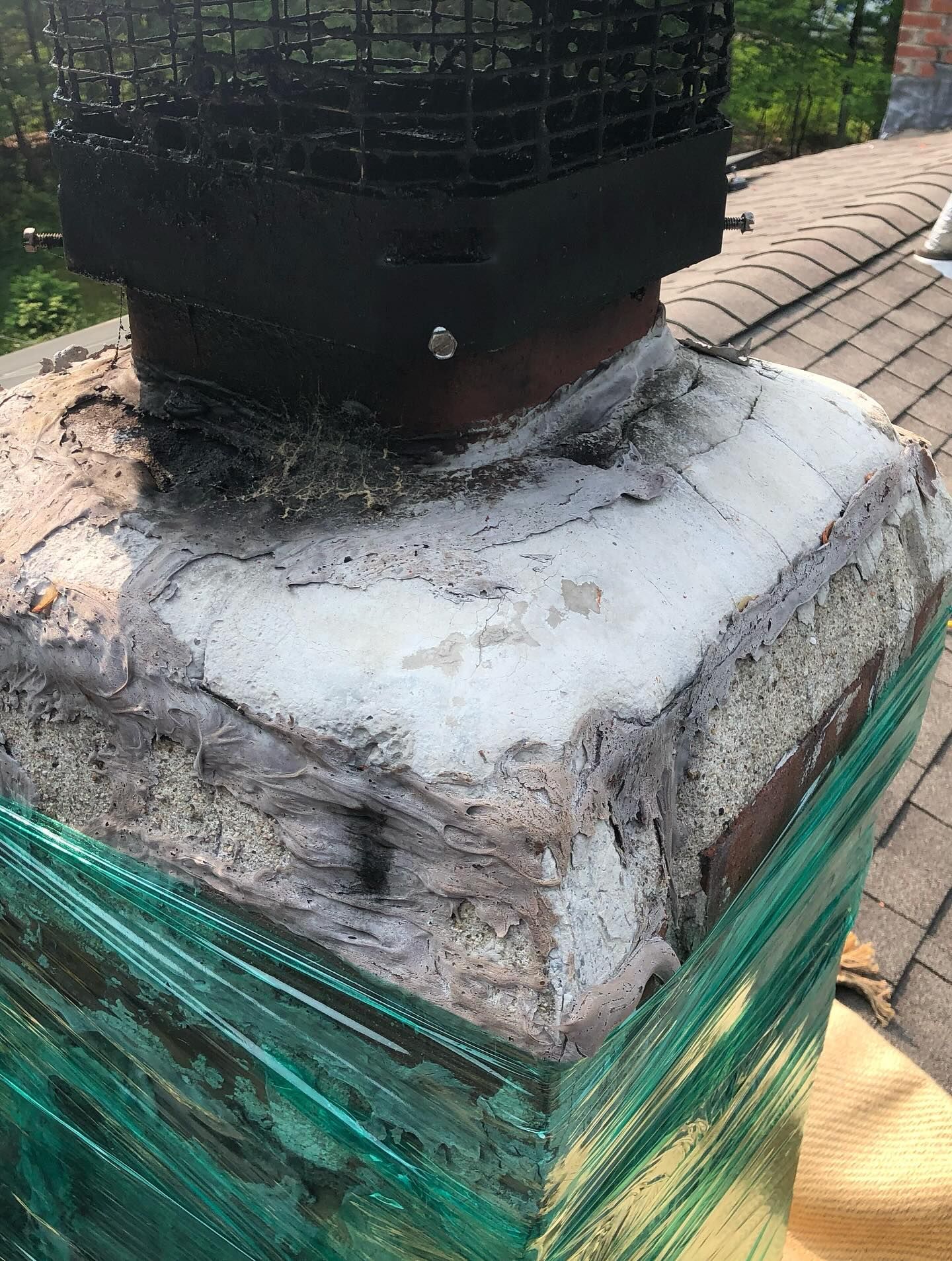 Damaged chimney with crumbling mortar and protective wrapping on a rooftop.