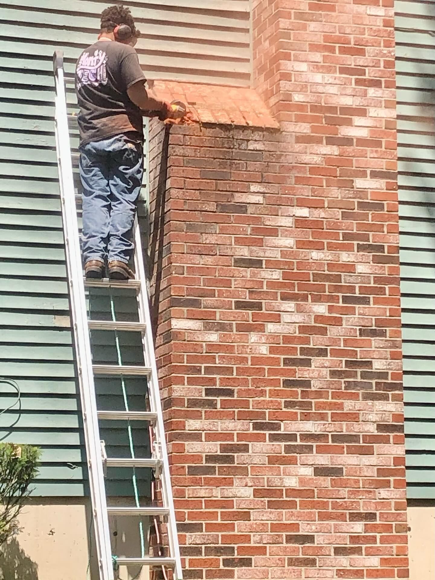 Person on ladder cutting top of brick chimney with power saw.