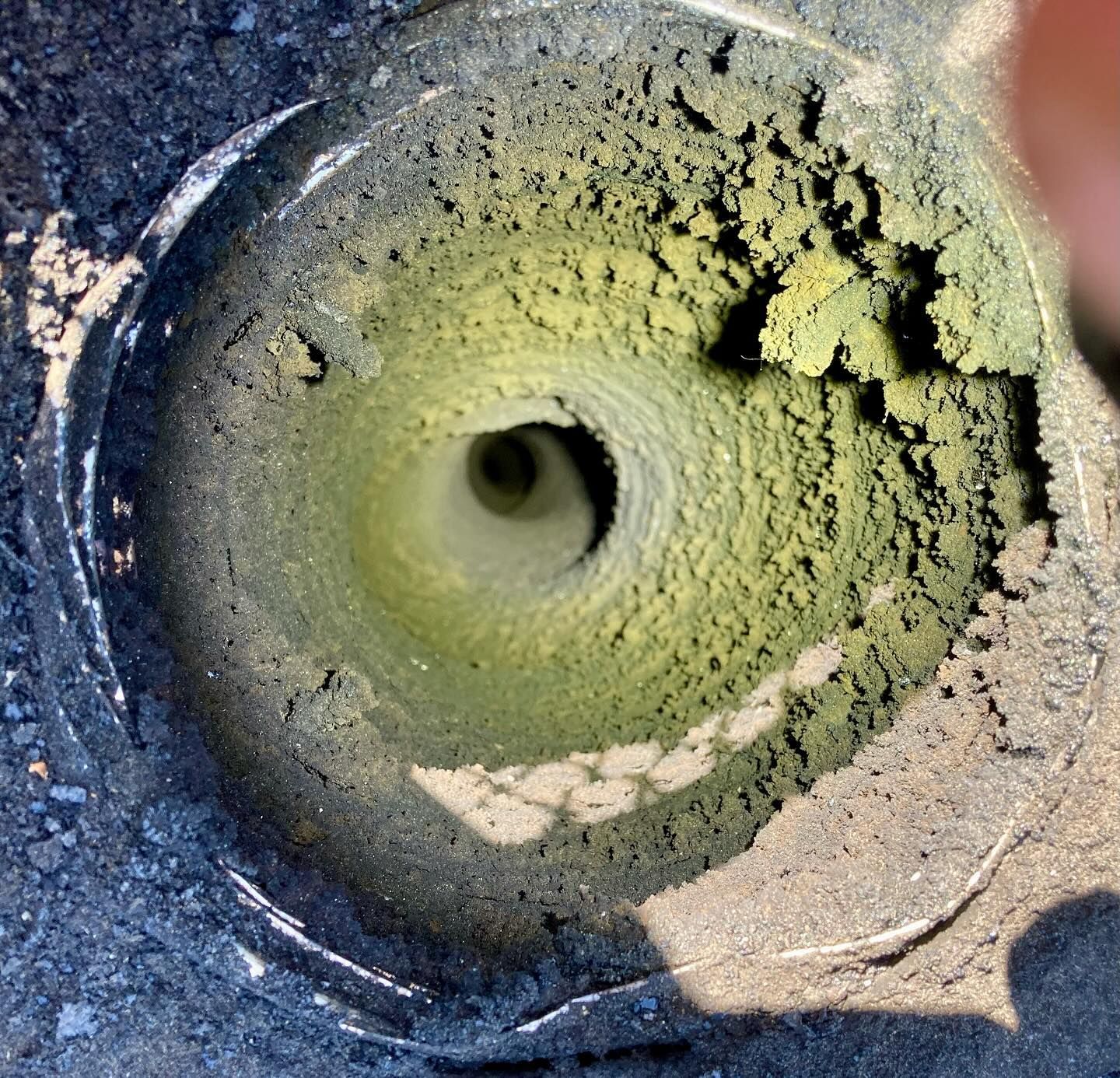 Hole drilled into ground, showing layers of sand and greenish material inside.