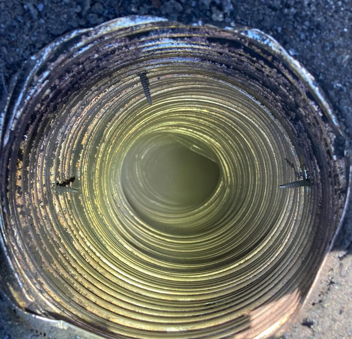 Inside view of a metallic, spiral dryer vent covered in black lint and debris.