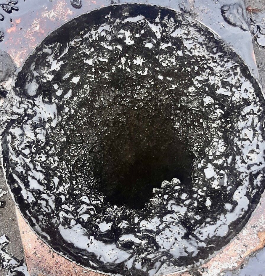 Black and gray melted material in a circular form, with a central hole and textured surface.