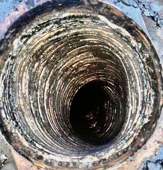 Inside view of a dark, dirty pipe. The pipe is cylindrical with visible spiral grooves and dark residue.