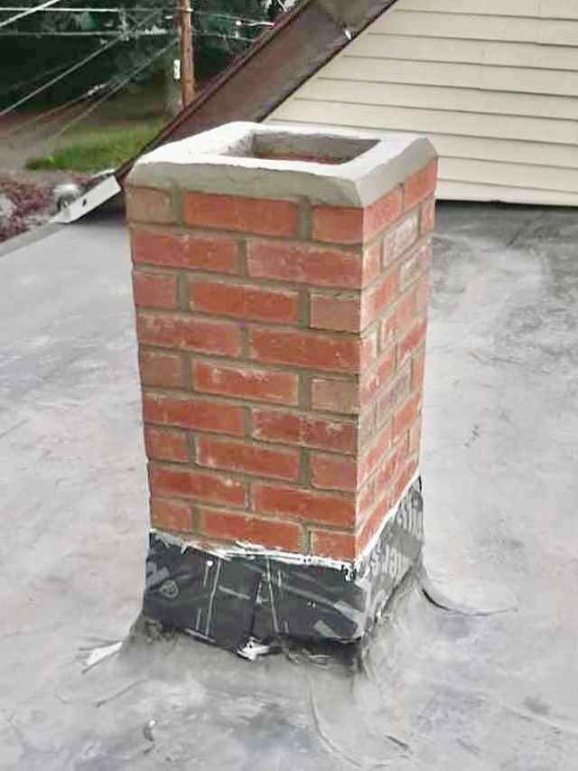 Brick chimney on a flat roof, sealed with dark flashing and a concrete cap.