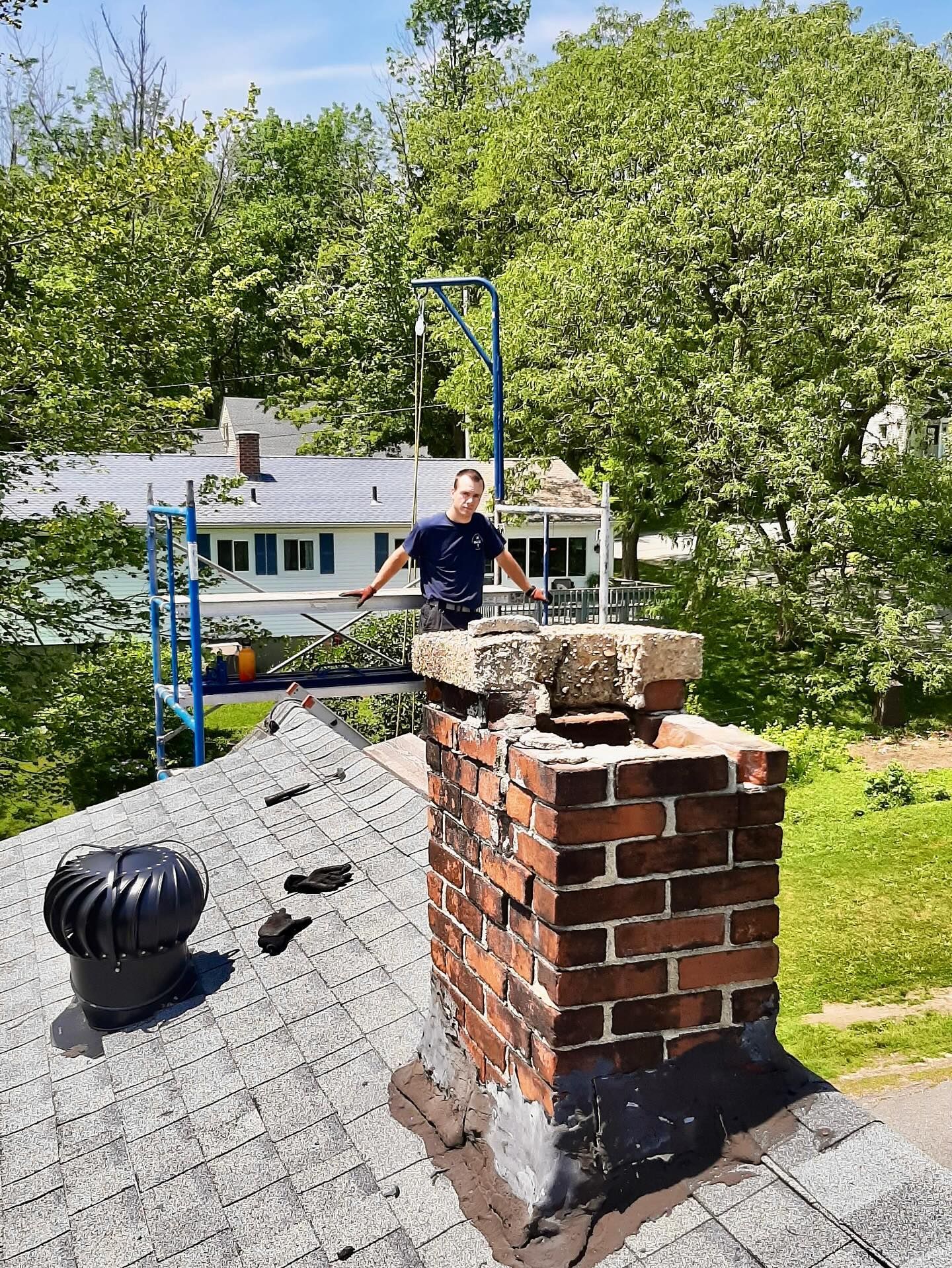 Man on a chimney top, arms outstretched, near a residential area. Chimney is made of brick.