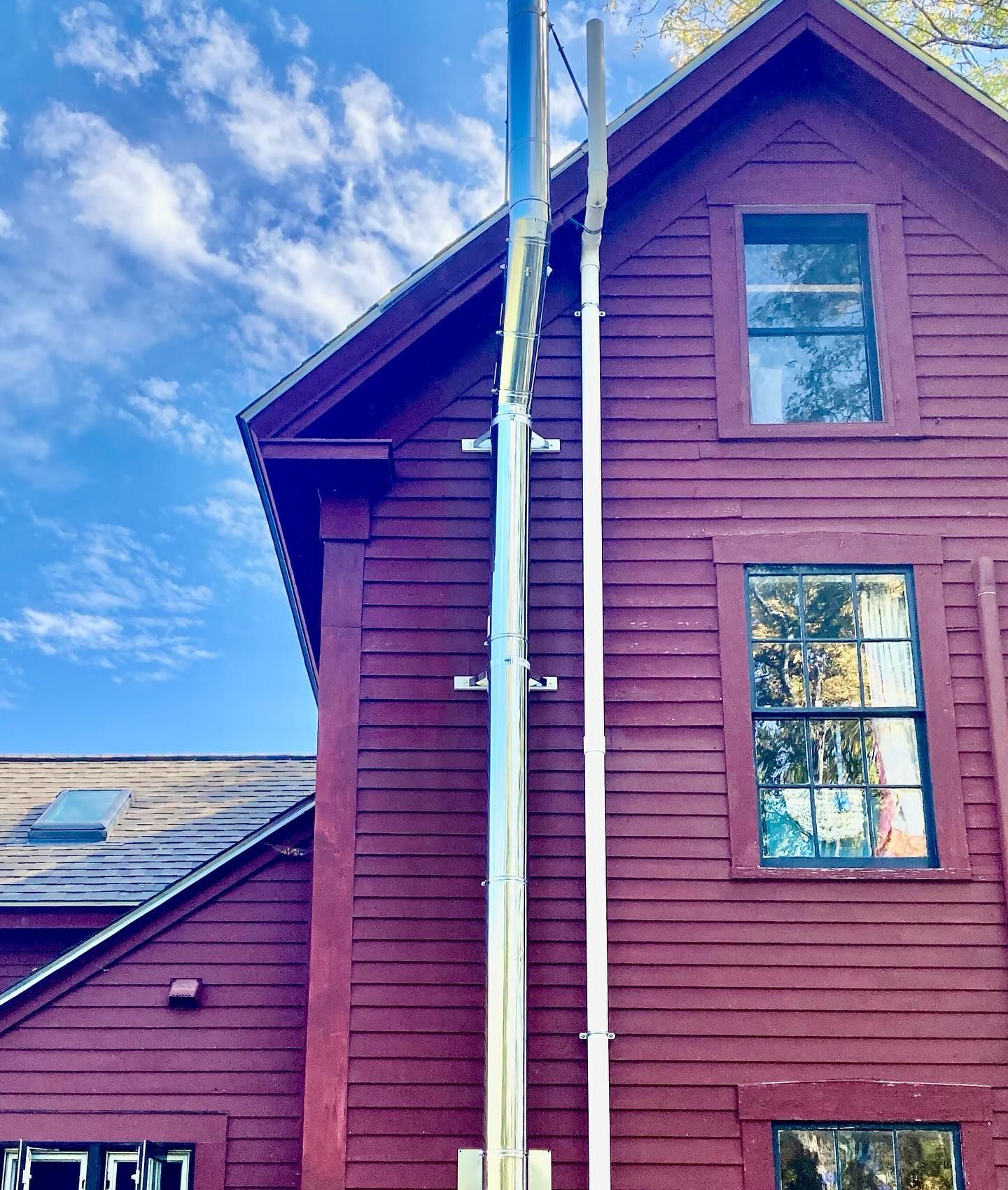 Two silver poles are mounted on the red side of a wooden building with windows. Cloudy sky.
