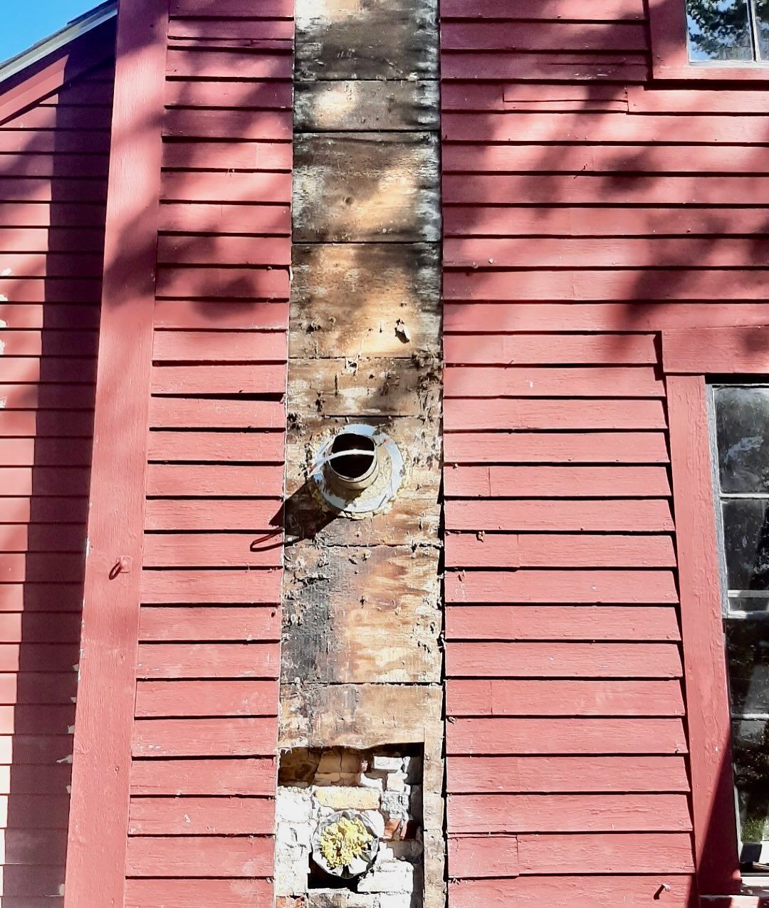 Exterior view of a red wooden building with a damaged chimney. Chimney is missing bricks in places.