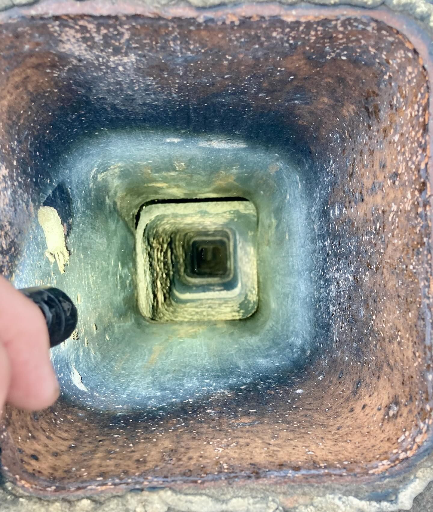 Looking up a chimney, showing a square flue within a square brick structure. Light reveals soot and a small square opening.