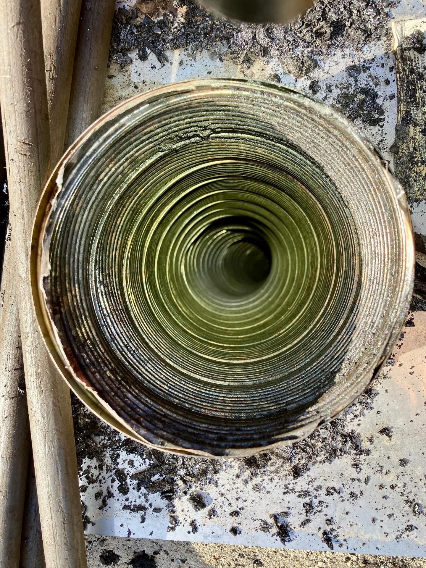 Looking down a green and silver insulated duct with debris around the opening.