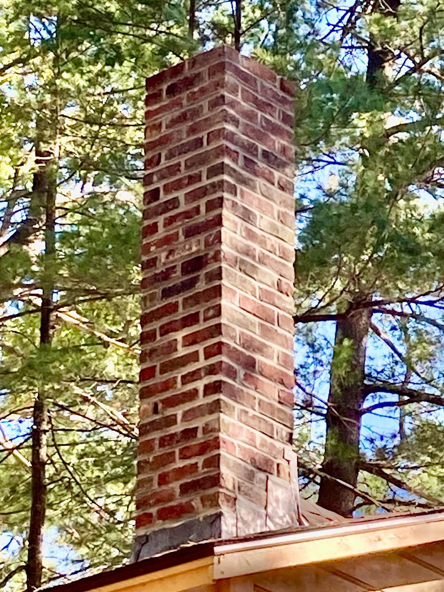 Tall brick chimney against a backdrop of green trees and blue sky.