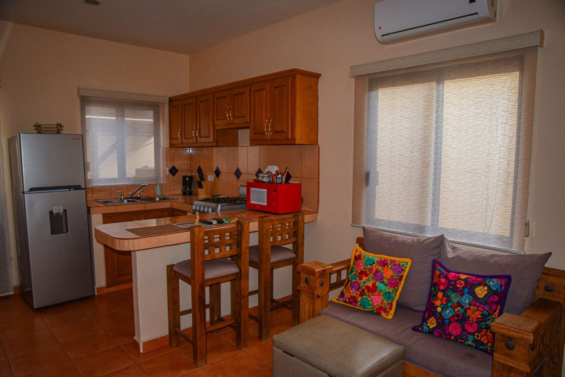 A living room with a couch , chairs , a refrigerator and a kitchen.
