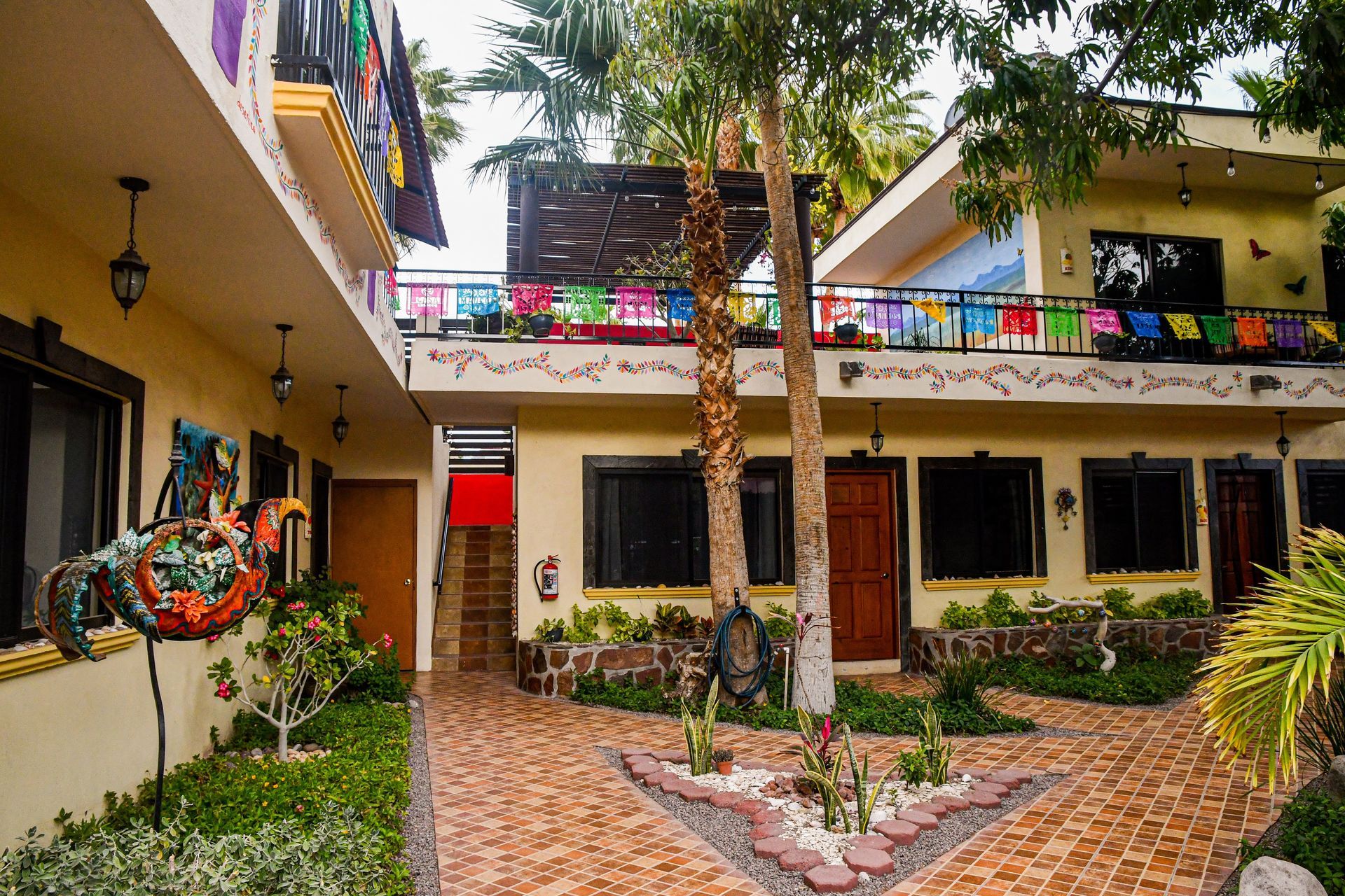 There is a brick walkway between two buildings with trees in the middle.