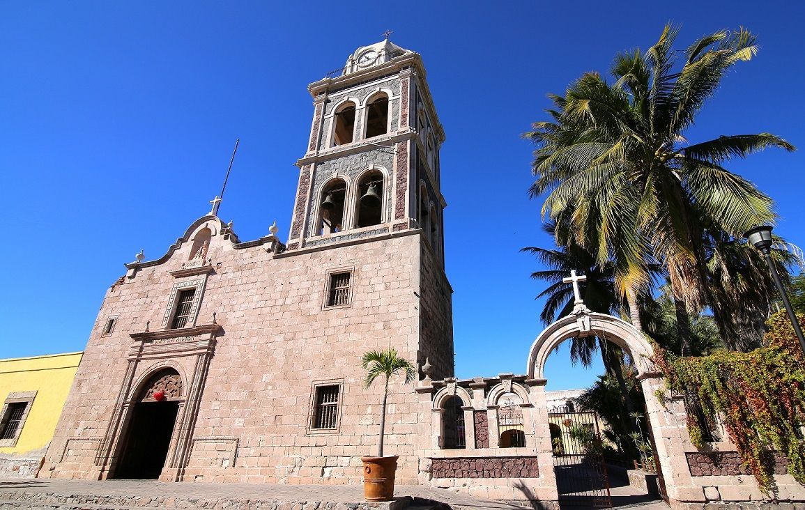 A church with a clock tower and a palm tree in front of it