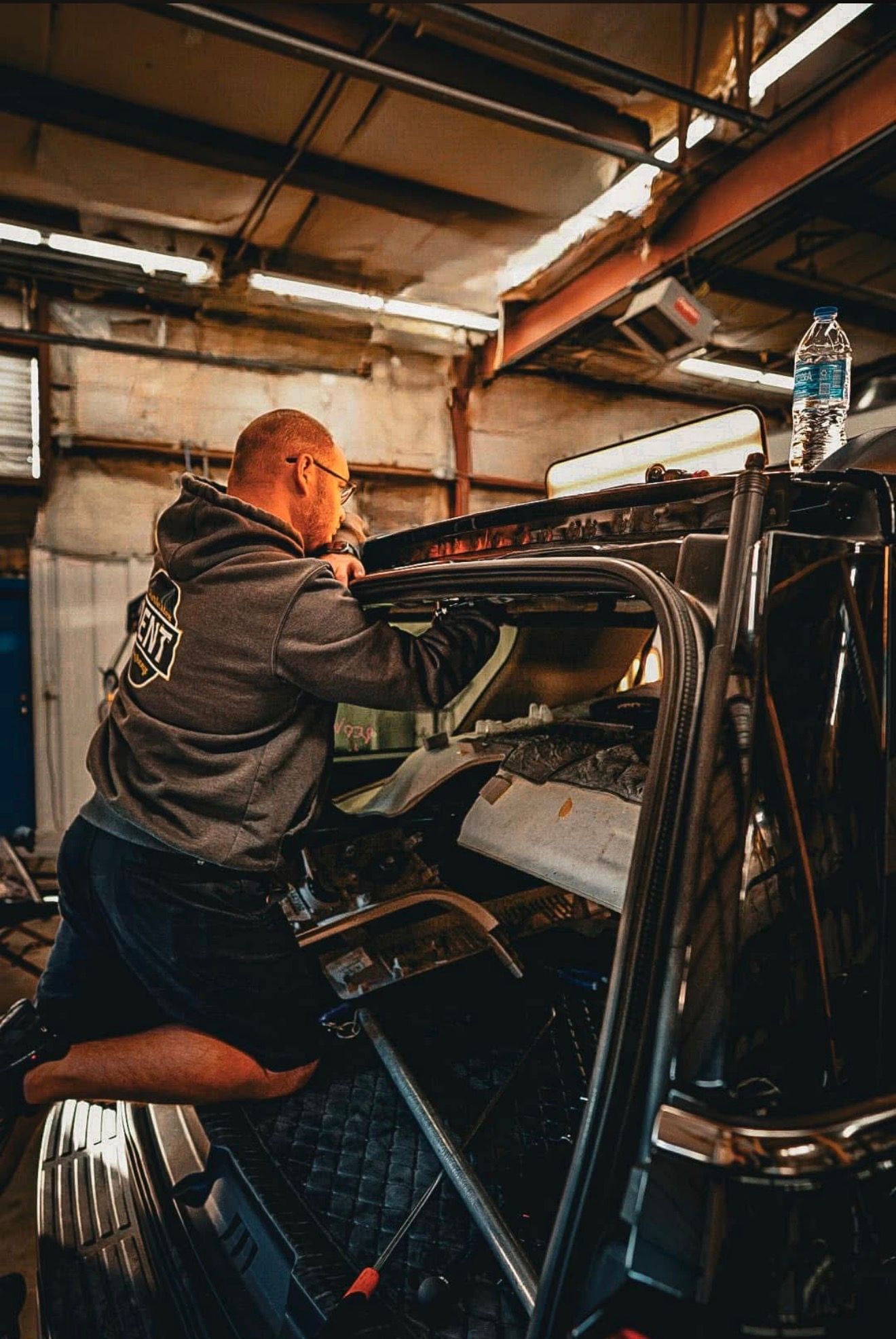a technician from The Charleston Dent Company wearing a grey hoodie with the company logo, works intently on the interior of a black suburban roof in a well lit auto repair shop in Summerville,Sc. 