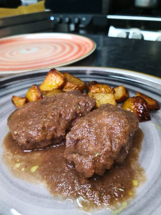 Due polpette di carne con sugo, patate arrosto, servite su un piatto.