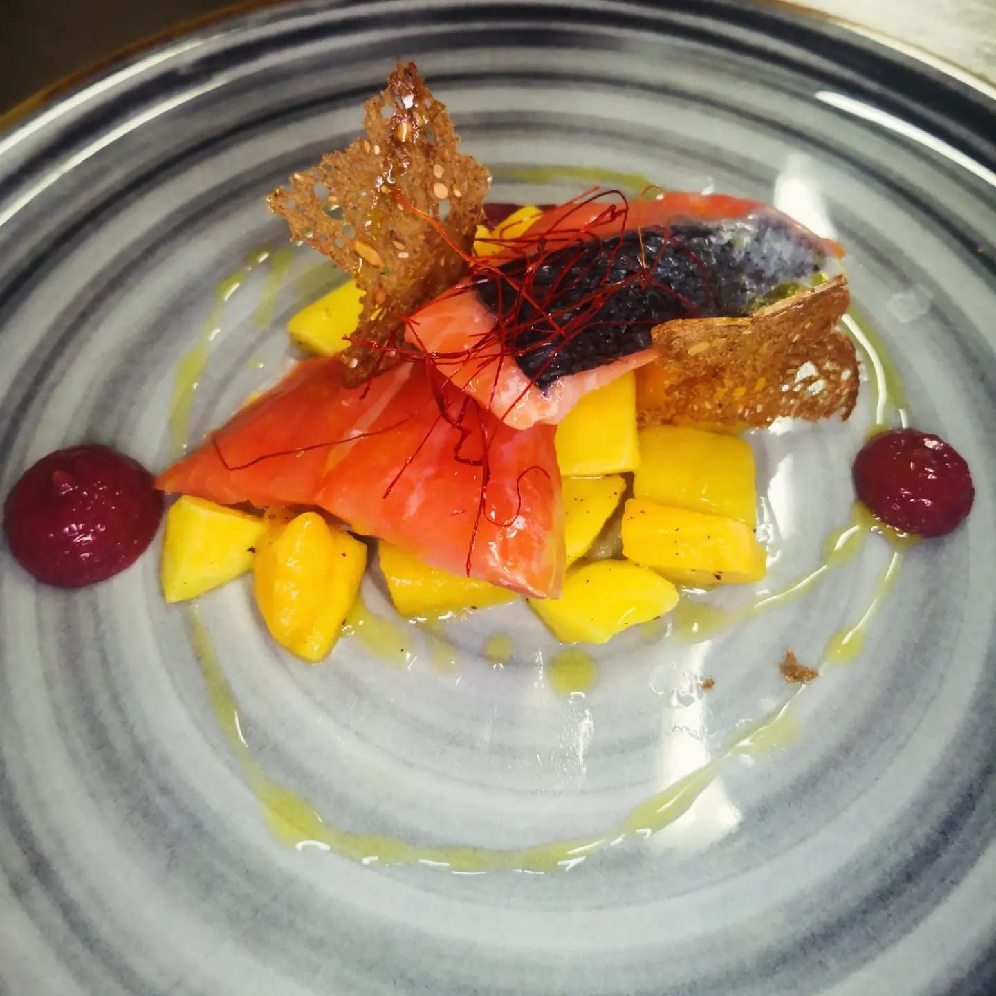 Insalata di salmone e mango su un piatto decorativo, guarnita con cracker croccanti e salsa rossa.