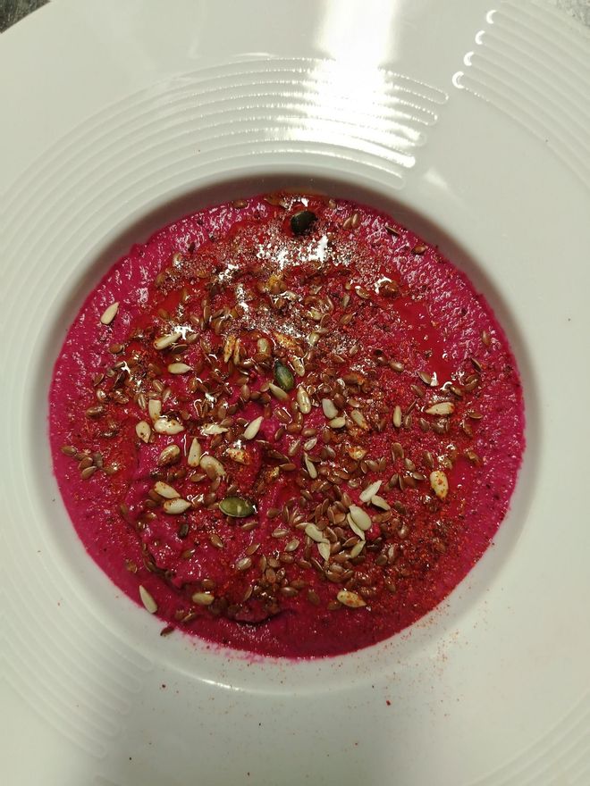 Zuppa di barbabietole in una ciotola bianca, guarnita con semi e noci.