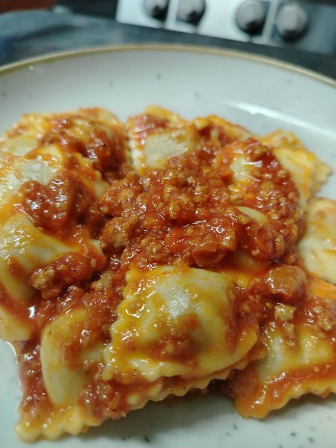 Ravioli al sugo rosso in una ciotola bassa. La pasta è condita con una salsa di pomodoro densa.
