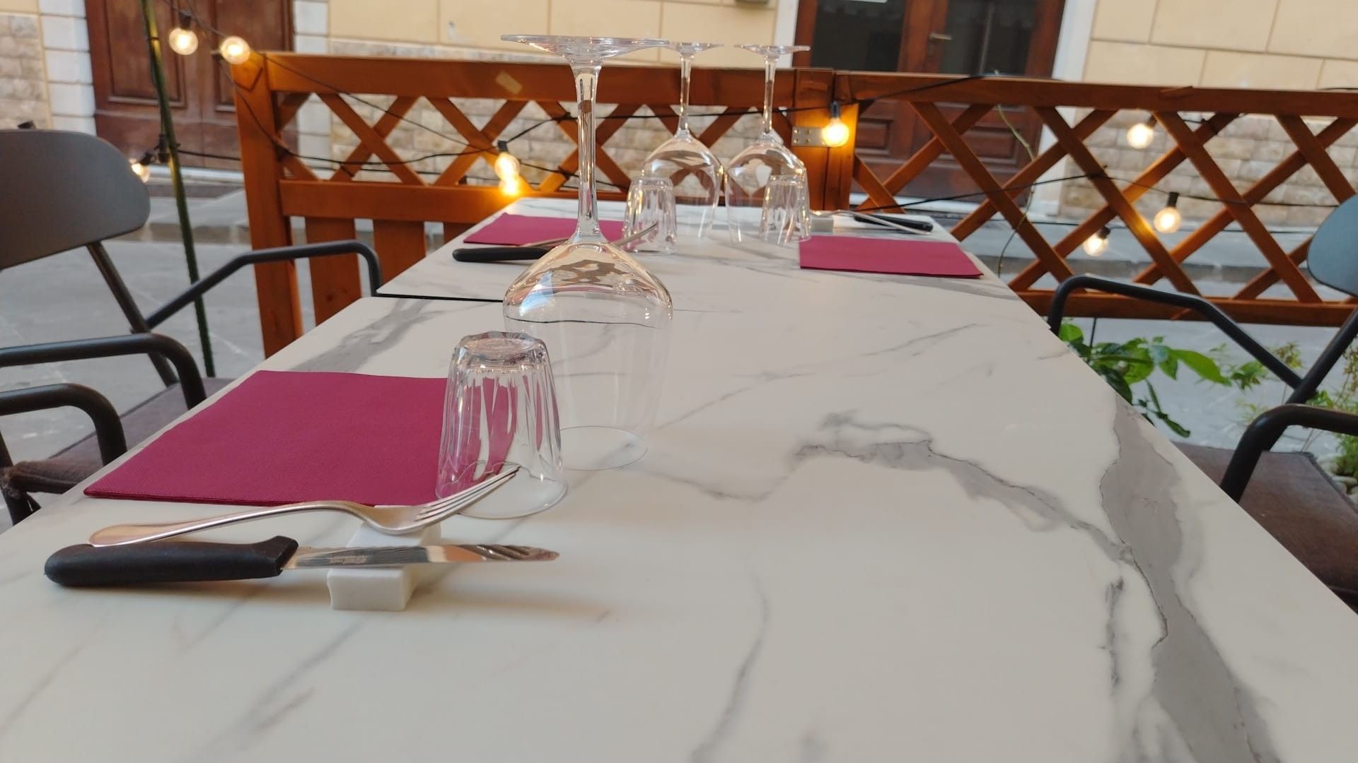 Tavolo apparecchiato per cenare all'aperto con bicchieri, posate e tovagliette rosa.