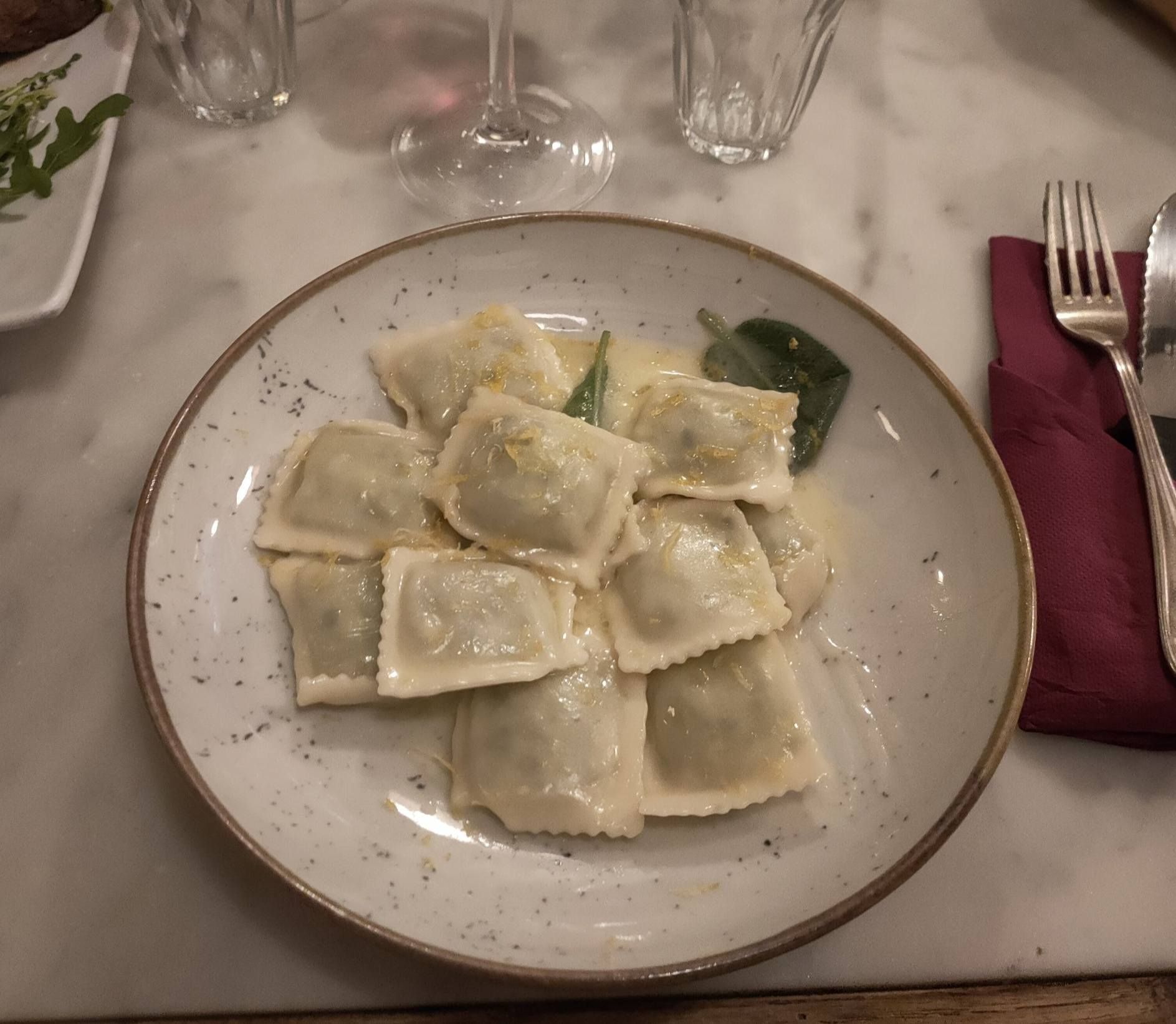 Piatto di pasta composto da ravioli quadrati in una salsa leggera, servito su un piatto bianco punteggiato.