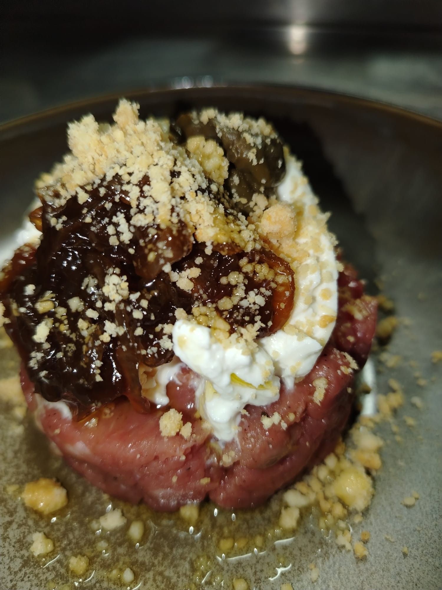 Piatto rosa dalla consistenza cremosa, guarnito con crema bianca, confetture marroni e una copertura friabile in una ciotola grigia.