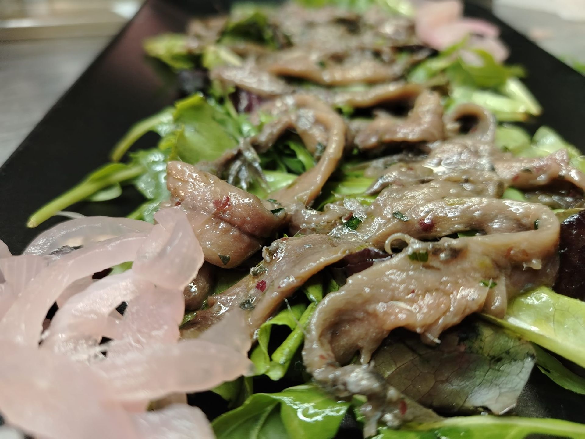 Insalata di acciughe: acciughe salate su verdure, con cipolle sottaceto, servite su un piatto nero.