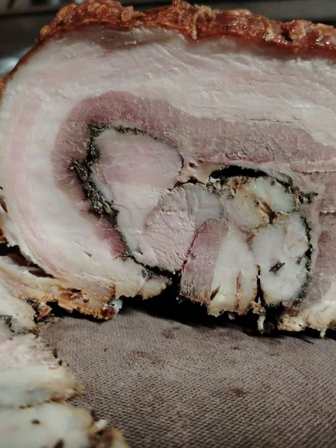 Primo piano di arrosto di maiale arrotolato e affettato, con pelle croccante e interno speziato.