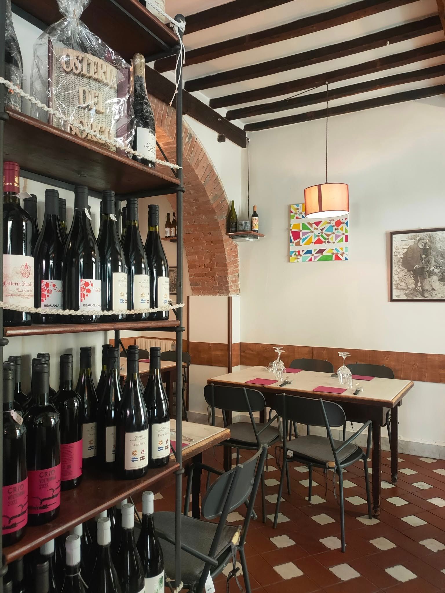 Interno di un'enoteca con scaffali pieni di bottiglie, un tavolo da pranzo e opere d'arte alle pareti.