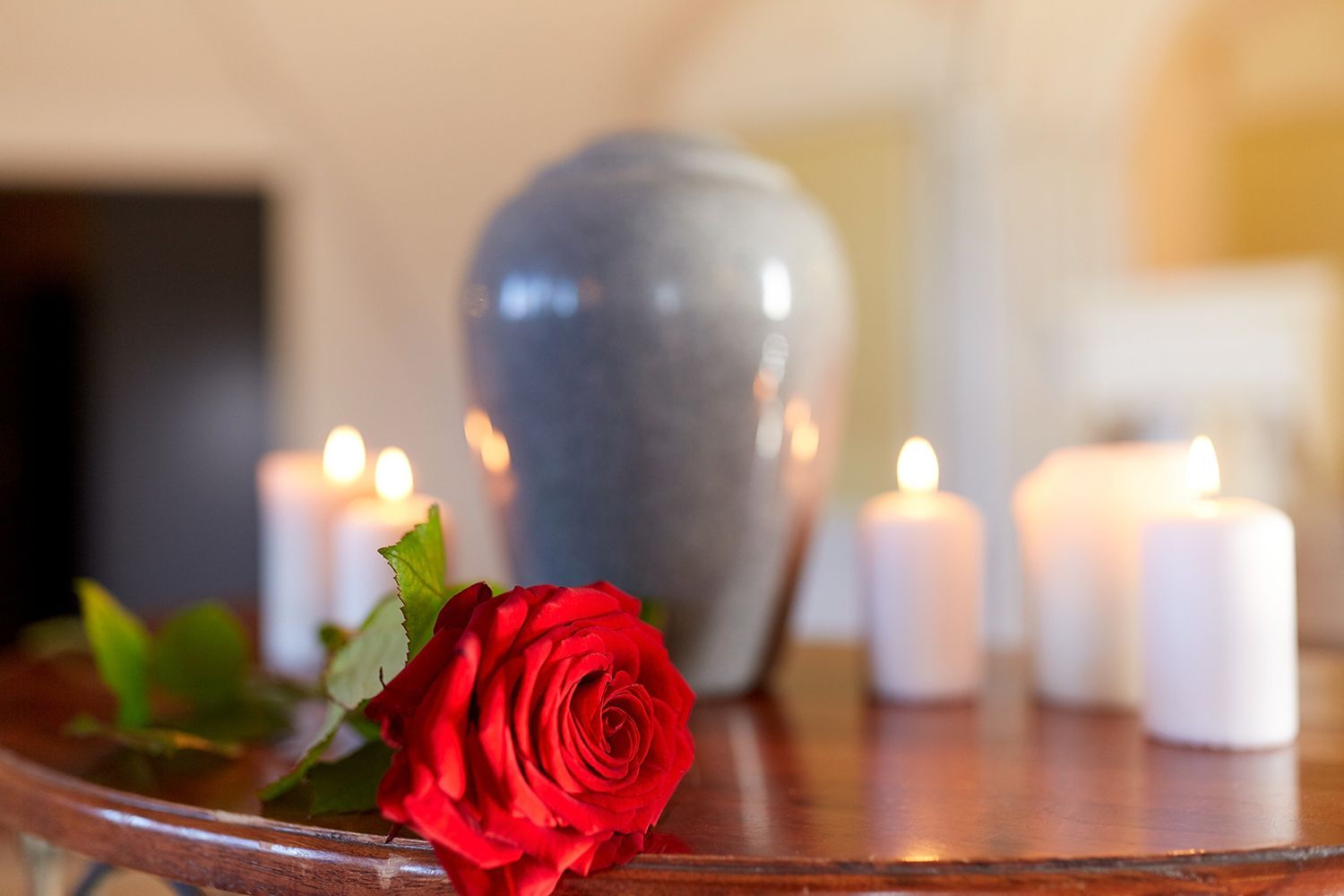 Red rose and cremation urn with burning candles.