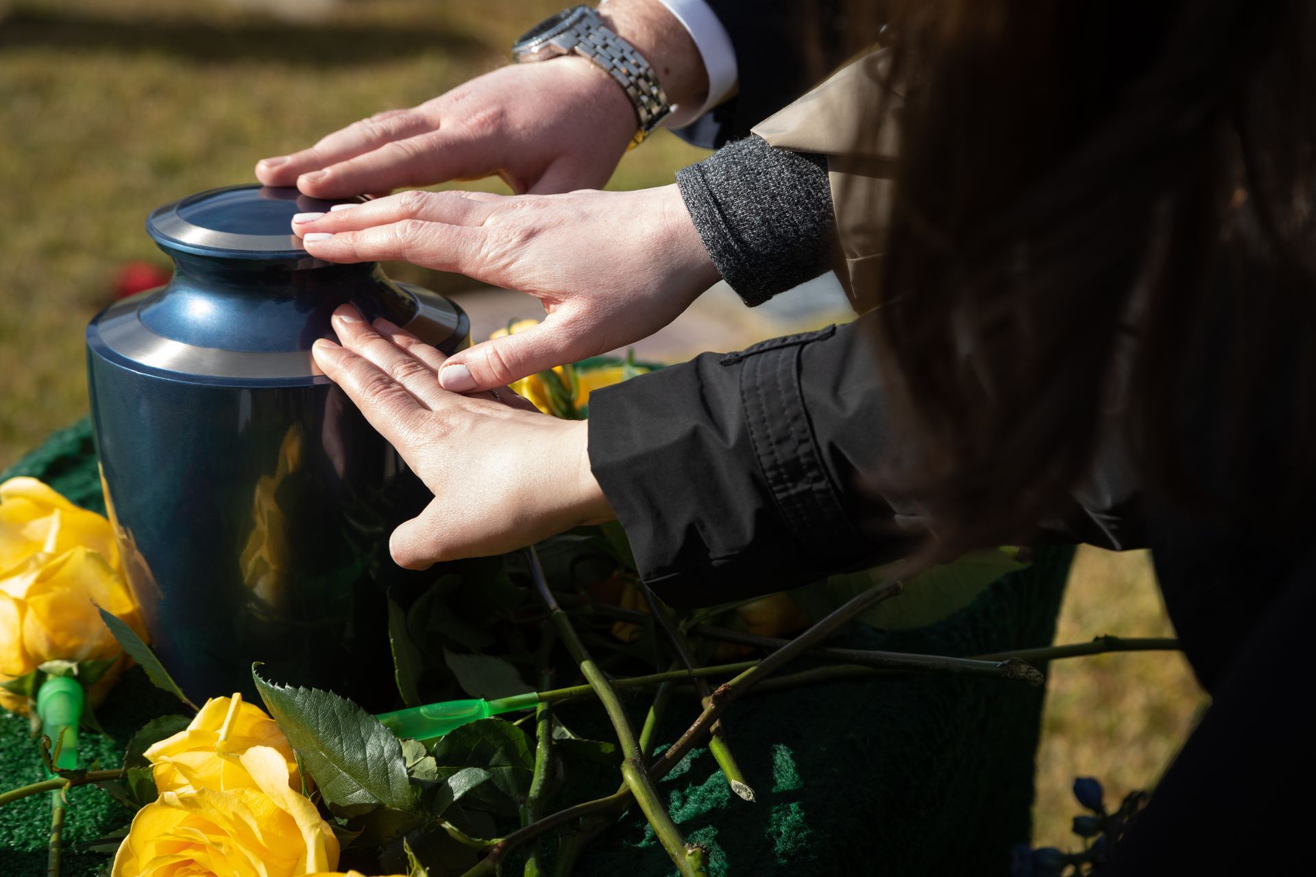 Three hands touching a cremation urn at a funeral.