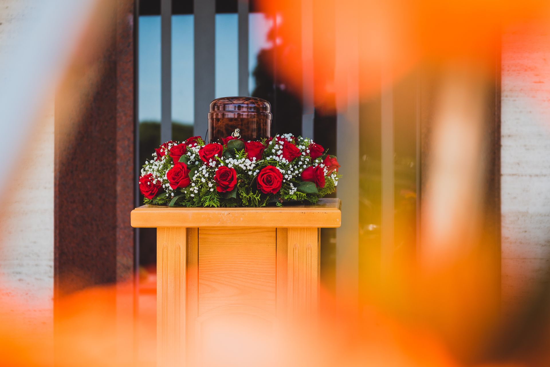 Urn on a wooden stand surrounded by red roses