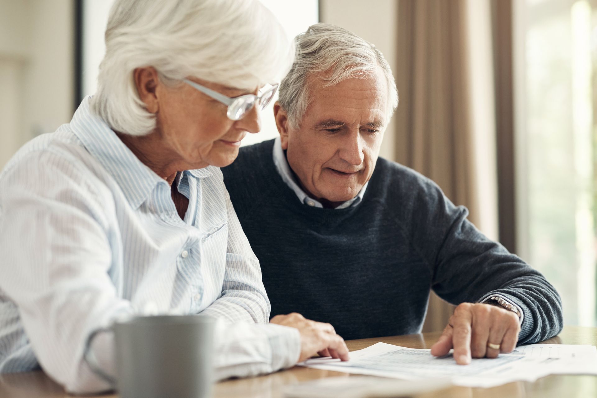 Senior couple reviews paperwork at a table; one points, both focused.