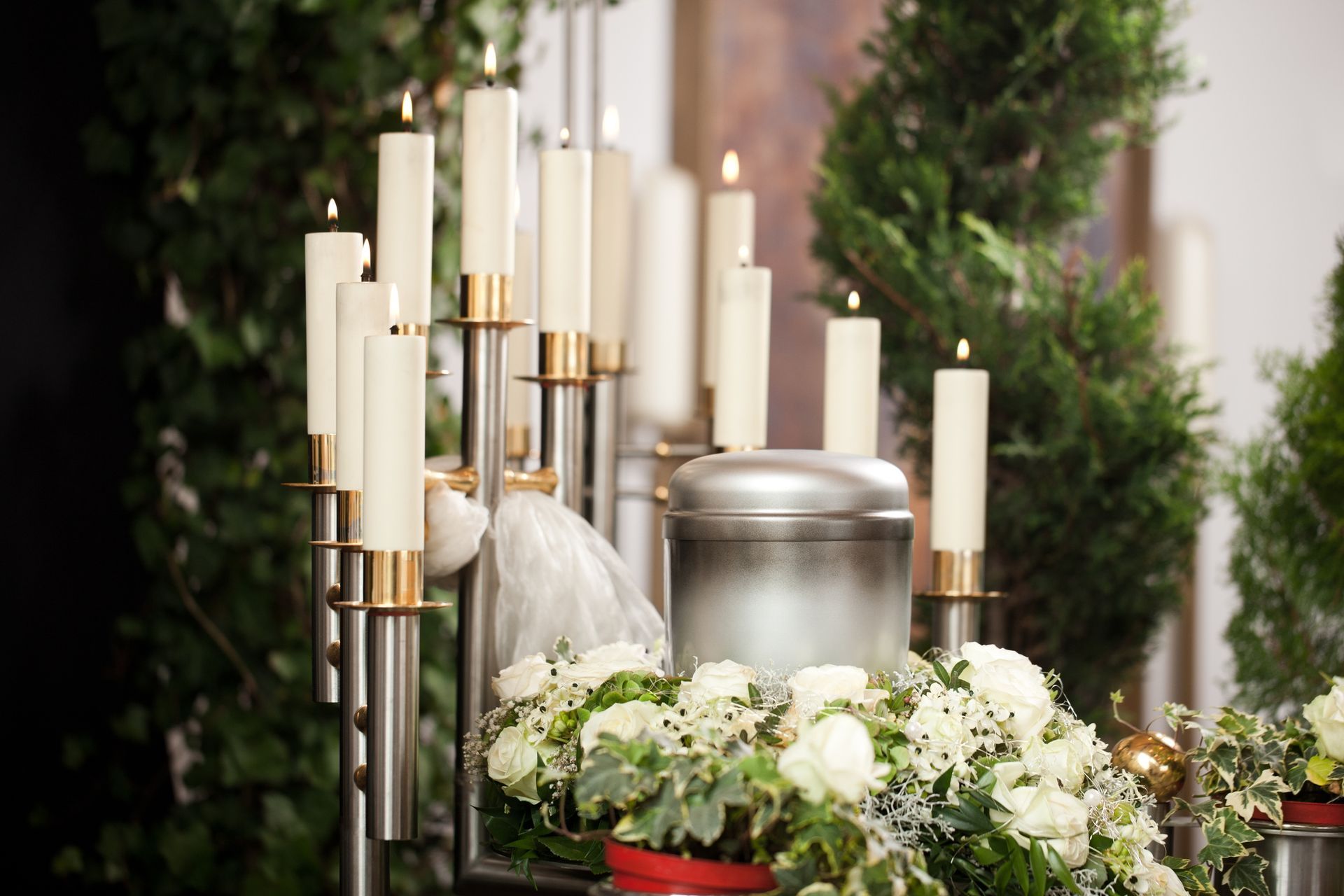 Silver urn surrounded by lit candles and white flowers, with greenery in the background.