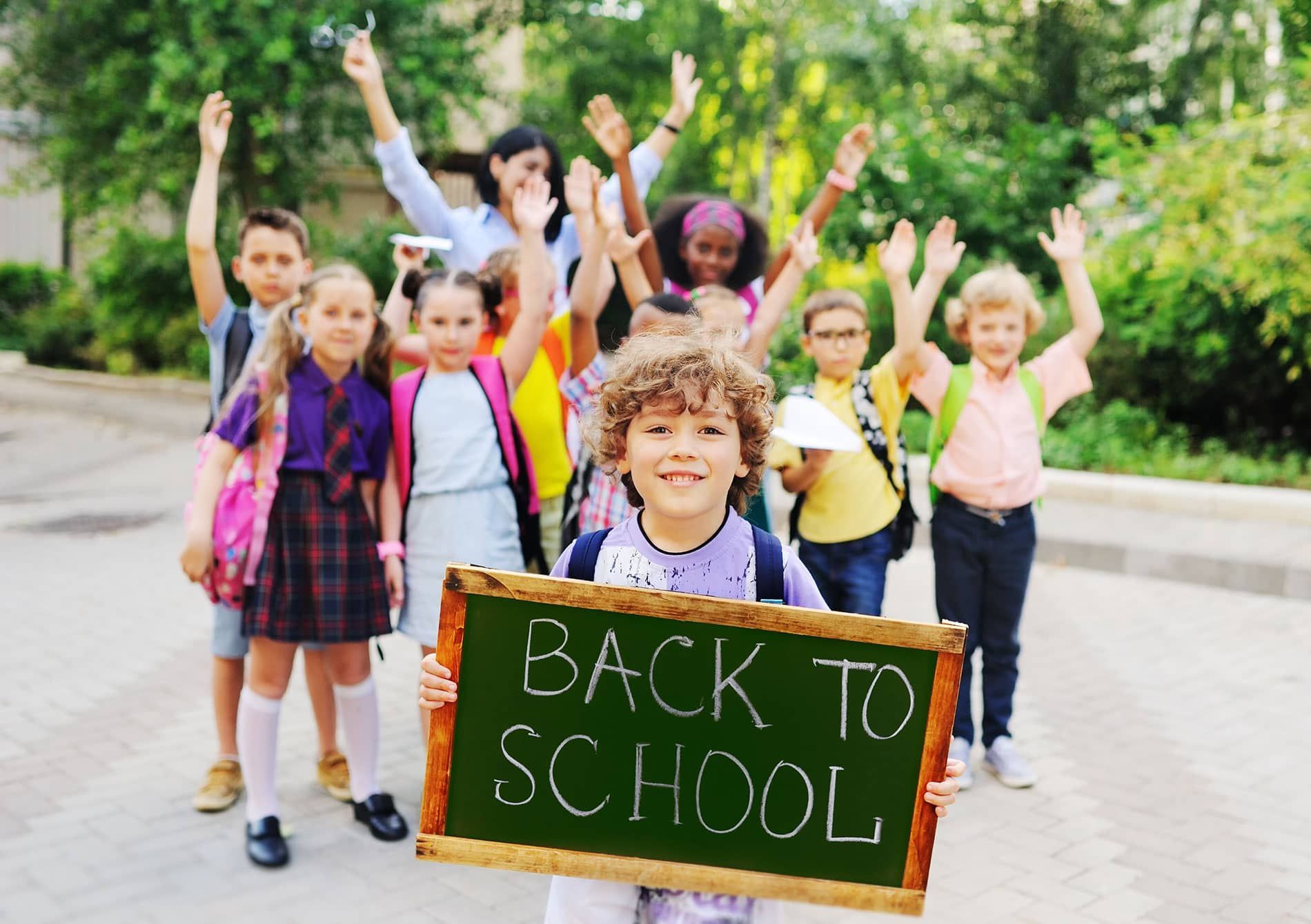 A boy is holding a sign that says back to school in front of a group of children.