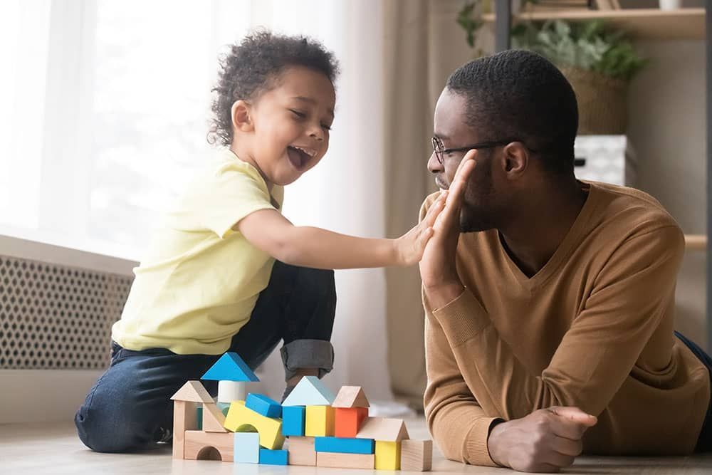A father and child play with building blocks, giving each other a high five.