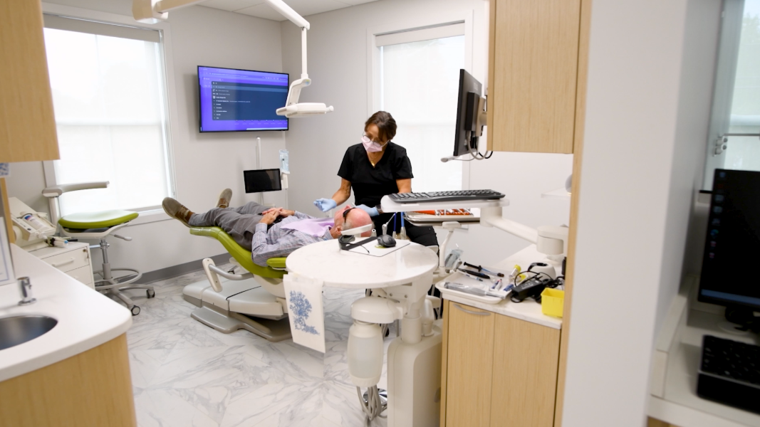 Dentist examining a patient in a dental office. Patient reclined in chair, doctor leaning over them.